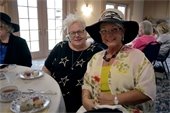 Two women wearing tea party attire and smiling into the camera