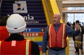 Ted Davis wearing an orange vest and explaining something to a group of people in construction helmets.