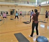 An instructor guiding a fitness class with a light dumbbell.